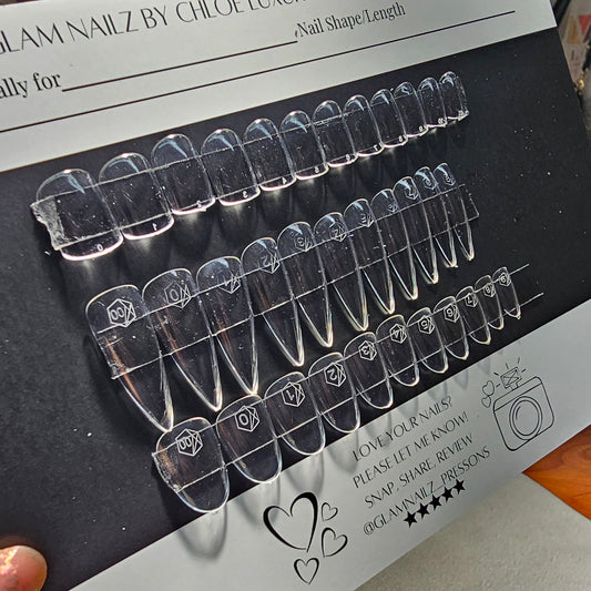 Set of clear nail extensions on a black card with branding details.