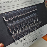 Set of clear nail extensions on a black card with branding details.