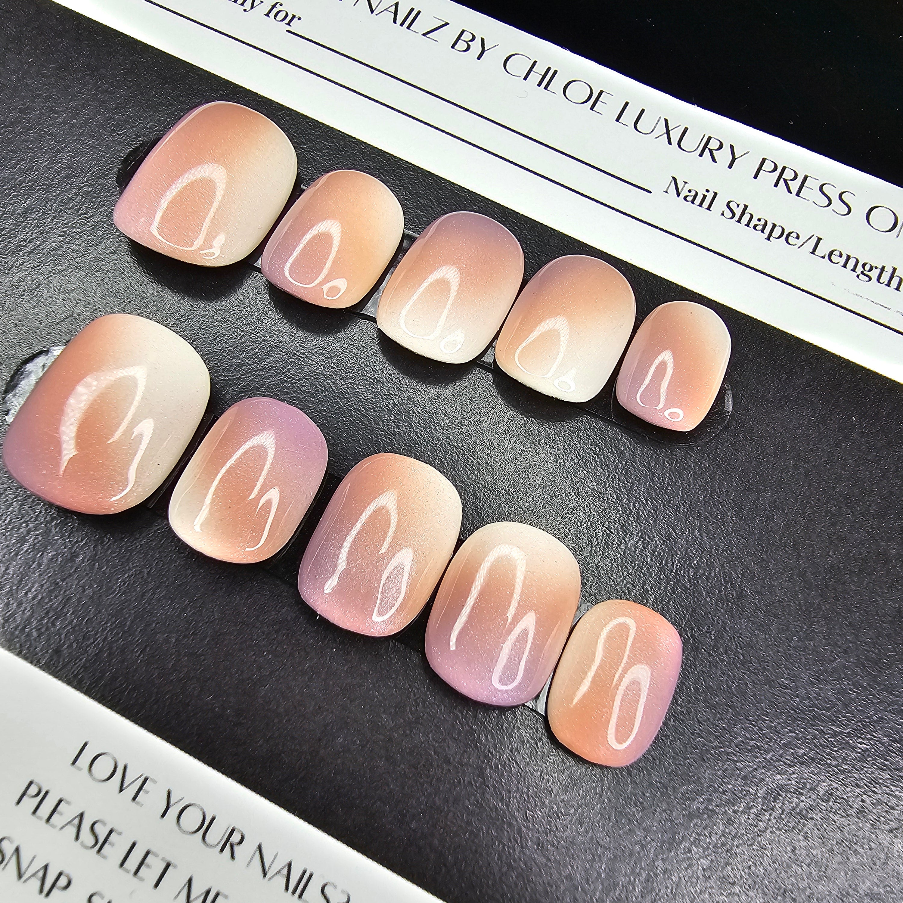 Set of press-on nails with a gradient design on a black surface with a branded box.