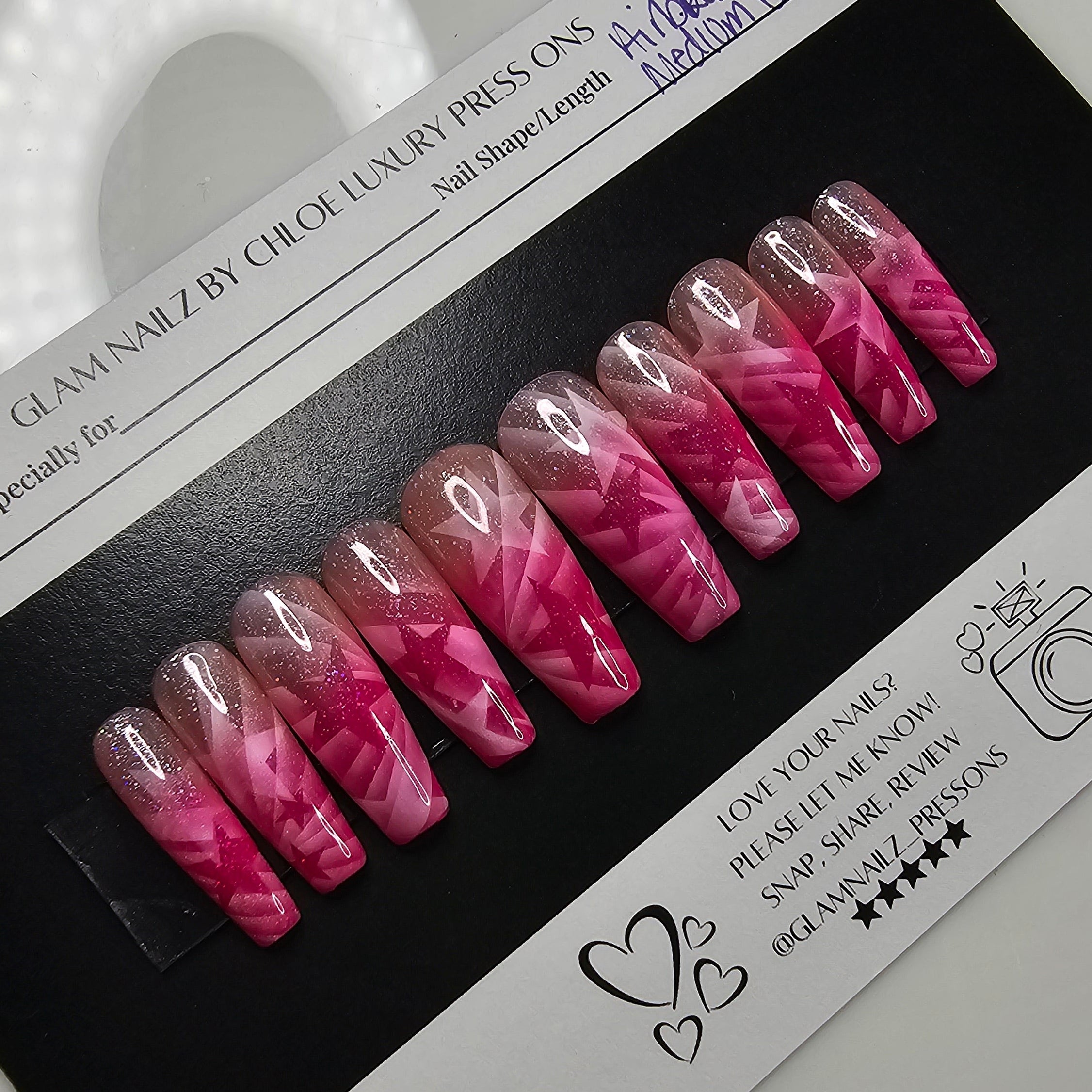 Pink and clear nail extensions on a black and white packaging with a ring light in the foreground.