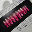 Pink and clear nail extensions on a black and white packaging with a ring light in the foreground.