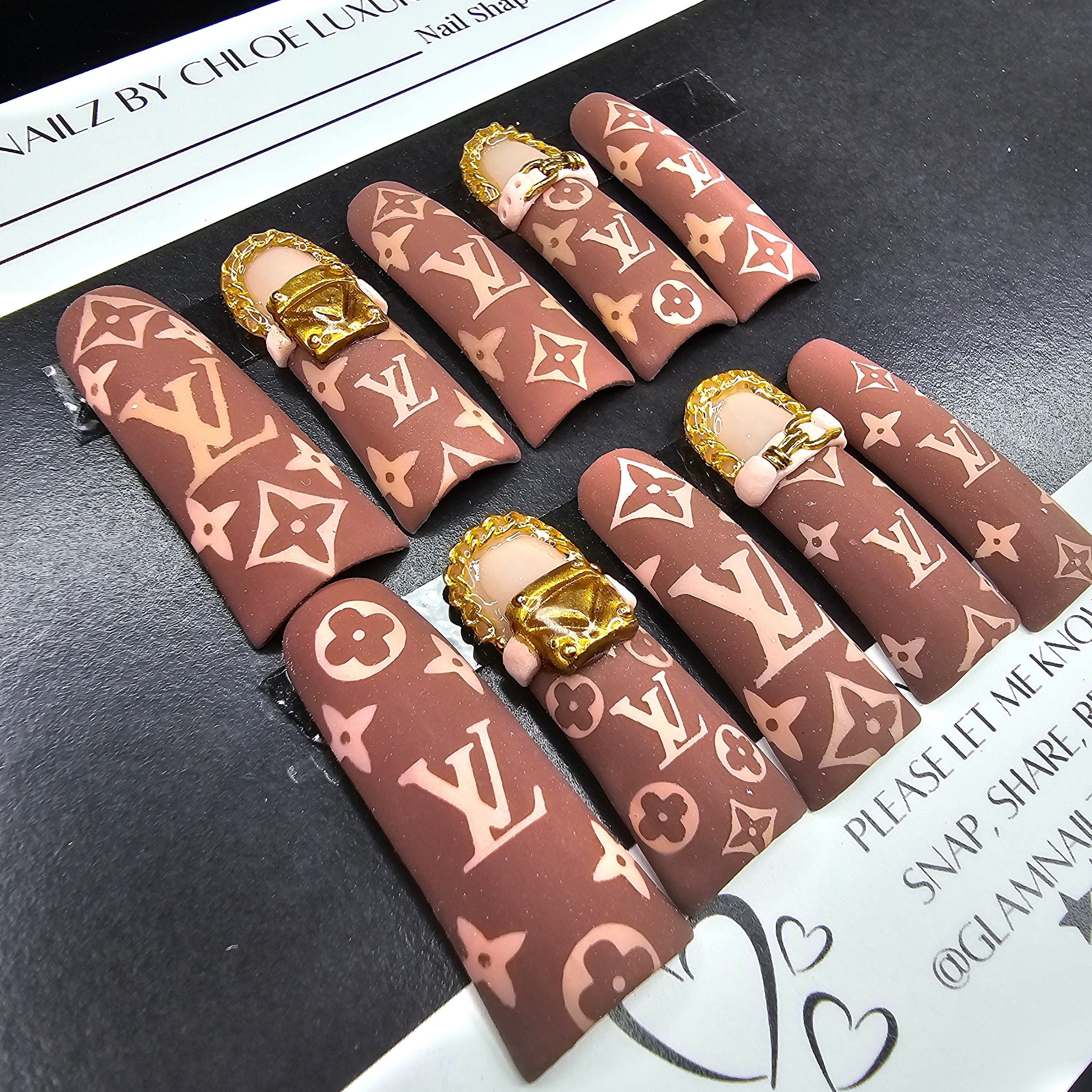 Nail art display with brown and gold patterned nails on a black surface.
