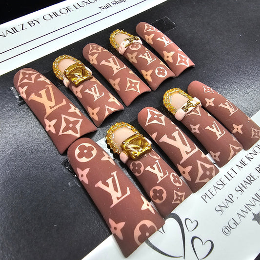 Nail art display with brown and gold patterned nails on a black surface.