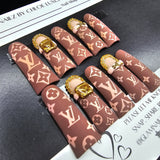 Nail art display with brown and gold patterned nails on a black surface.