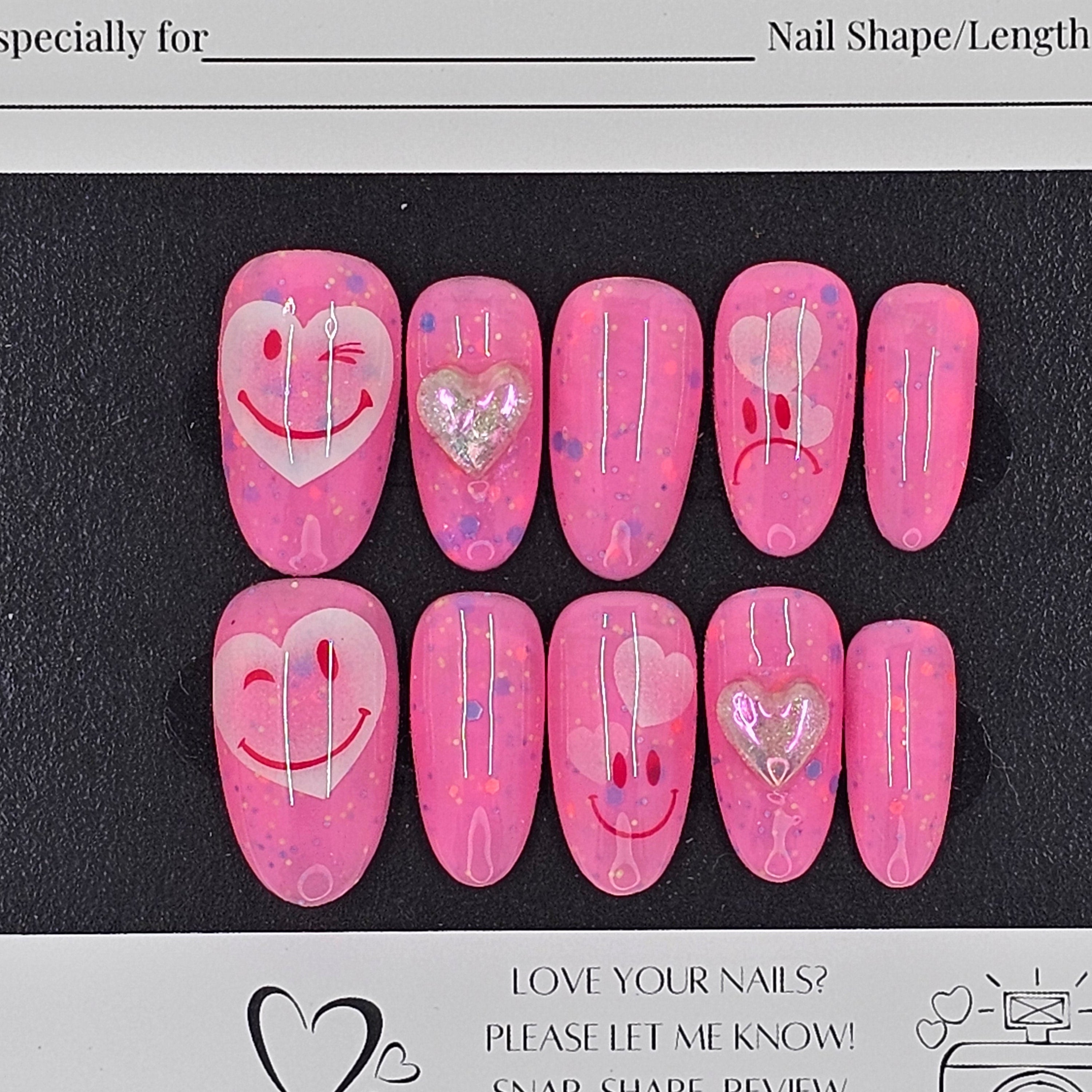 Set of pink press-on nails with heart designs on a black card with branding text.