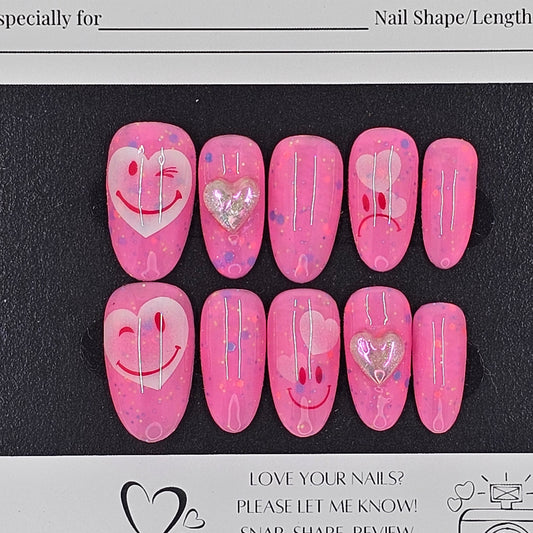 Set of pink press-on nails with heart designs on a black card with branding text.